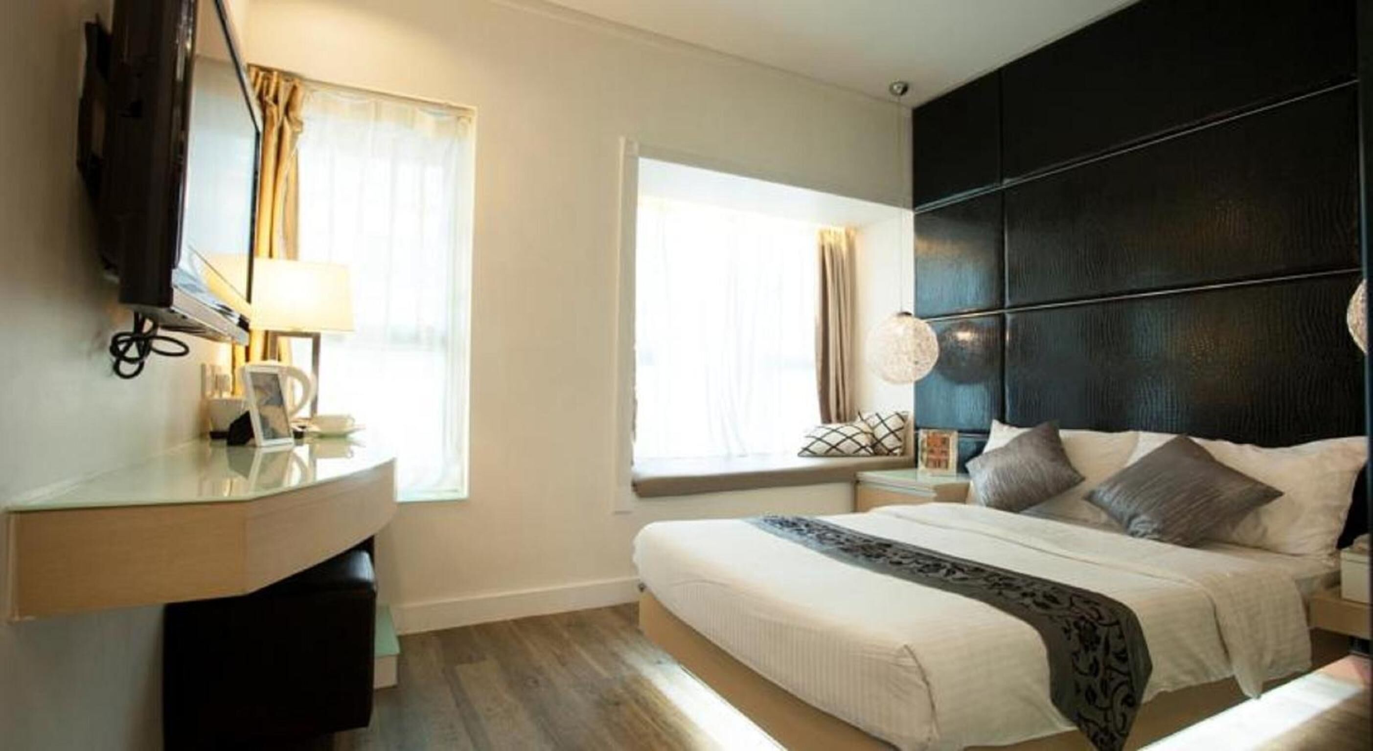 A hotel room with a bed, bedside tables, a desk with a lamp, and a TV.