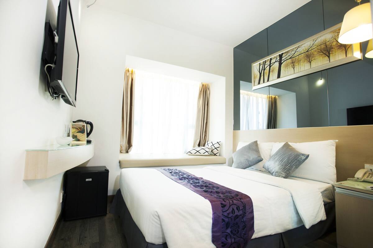 Una habitación de hotel con cama, mesita de noche, lámpara y televisor montado en la pared.