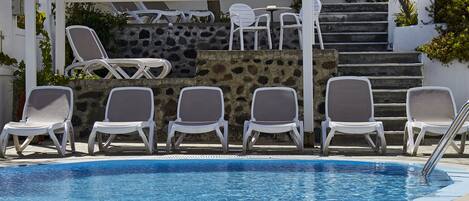Una piscina con sillas de descanso blancas y un muro de piedra al fondo.