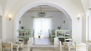 Uma ampla área de jantar com mobiliário branco e um lustre central.