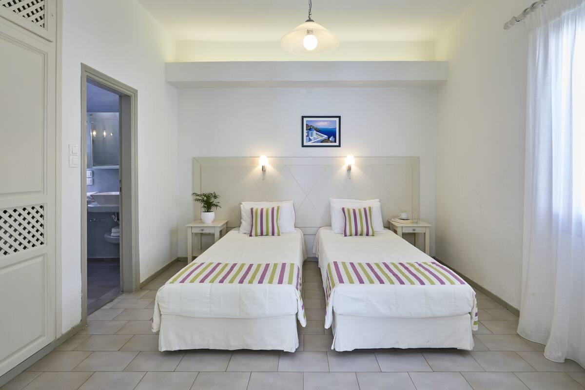 Habitació d'hotel amb dos llits, un quadre a la paret i vista al bany per una porta oberta.