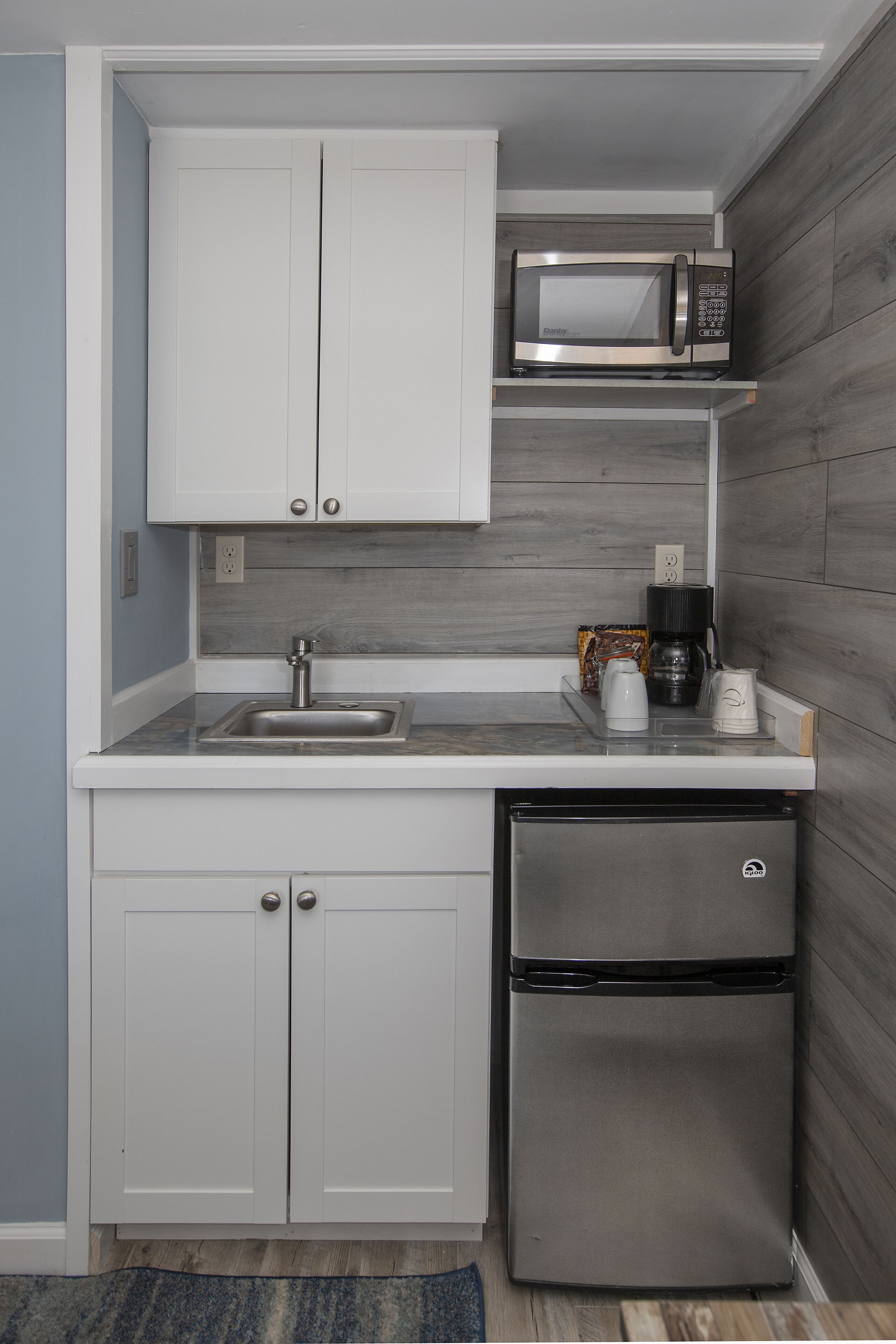 Cocina compacta con armarios blancos, refrigerador de acero inoxidable, microondas y cafetera.