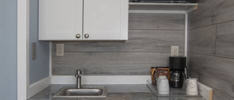 Cocina compacta con armarios blancos, refrigerador de acero inoxidable, microondas y cafetera.