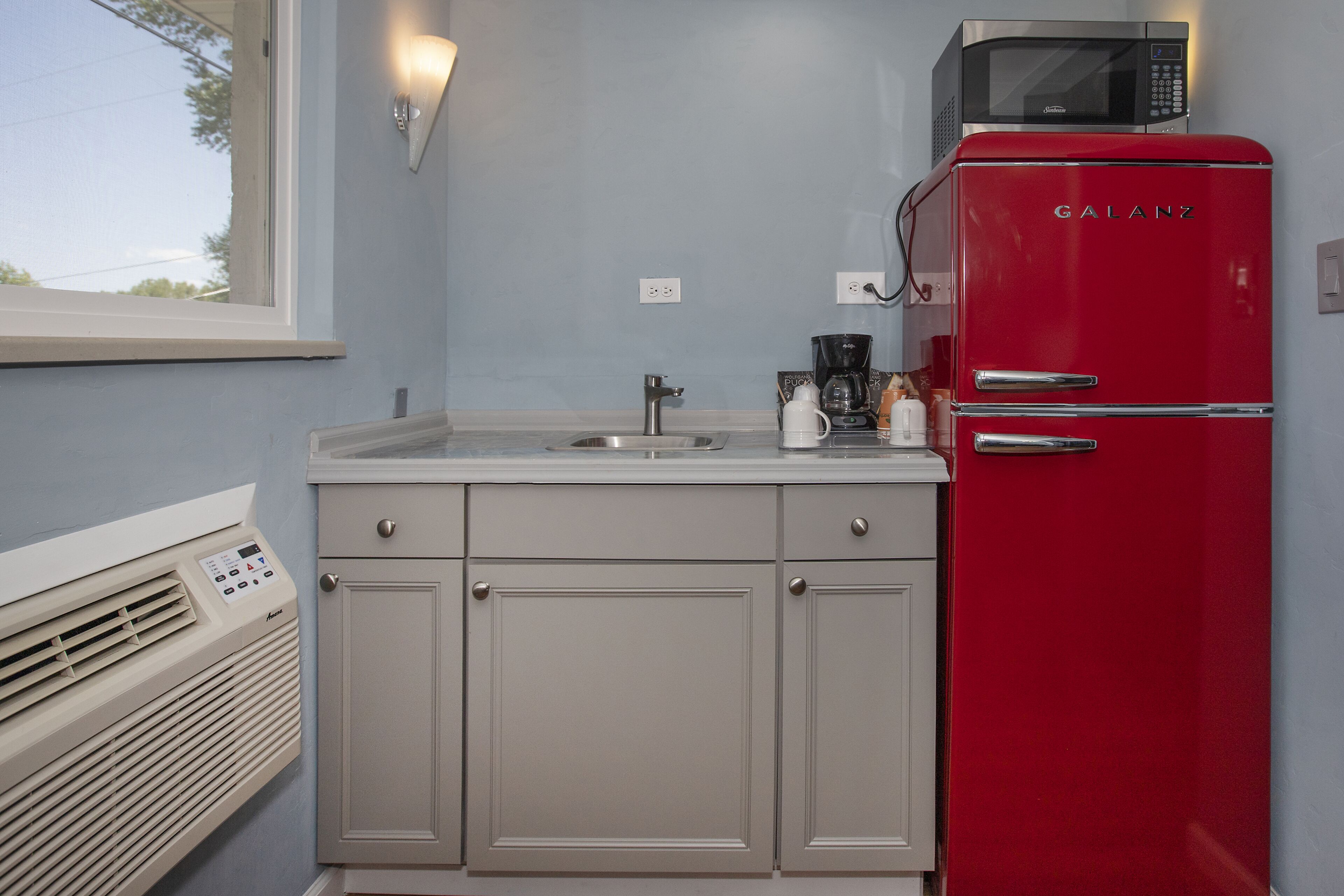 Una cocina compacta con un refrigerador rojo Galanz, un microondas integrado, un lavamanos y una cafetera.