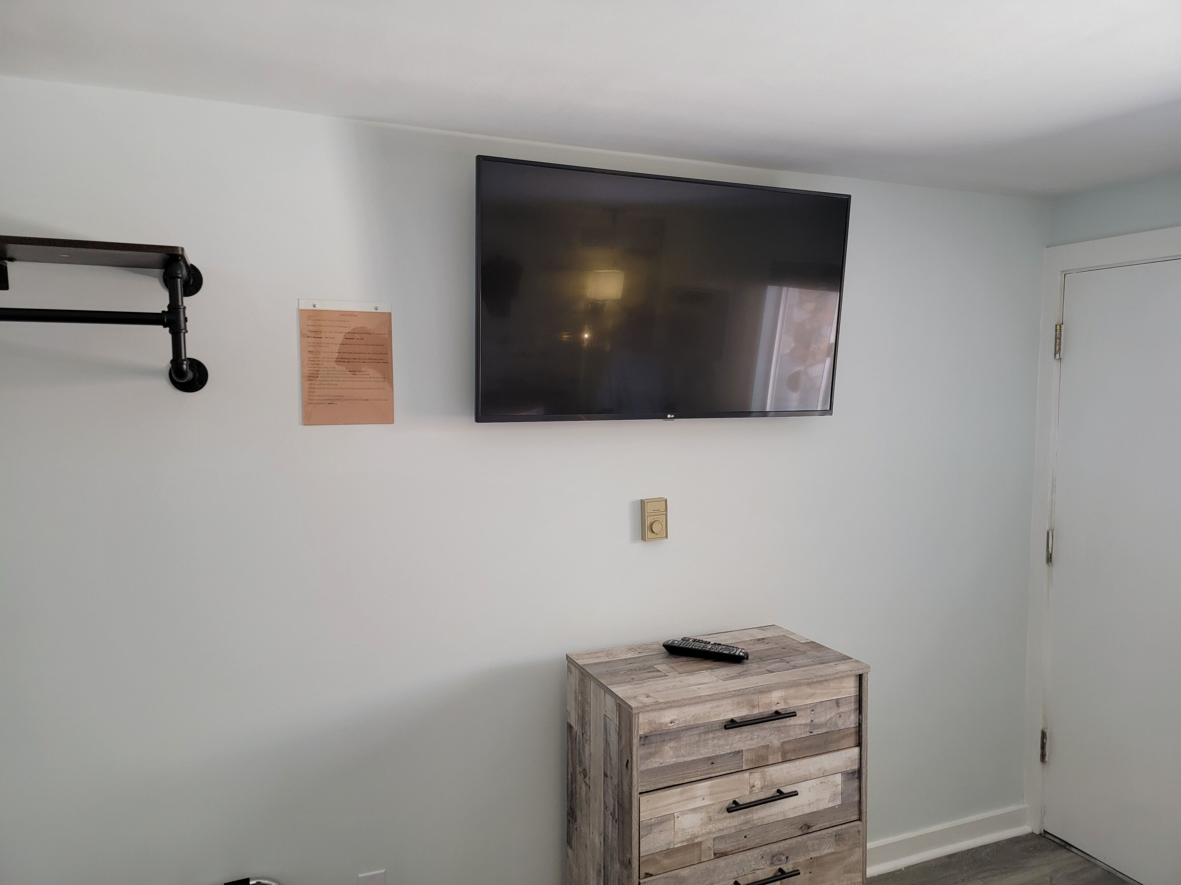 Una habitación con una televisión de pantalla plana montada, un aparador de madera, un mueble pequeño y una puerta.