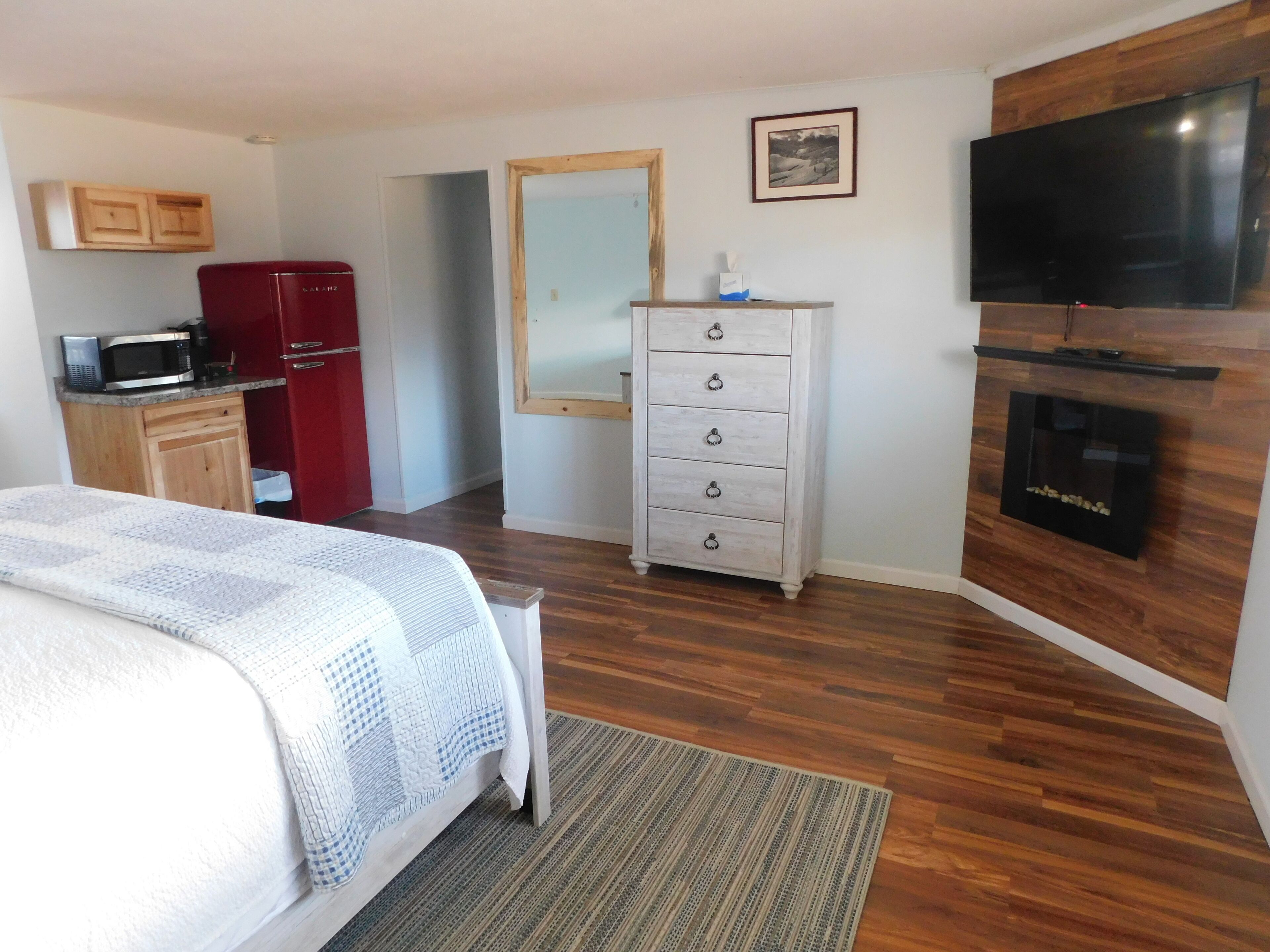A bedroom with a bed, a dresser, a television, a microwave, and a red refrigerator.