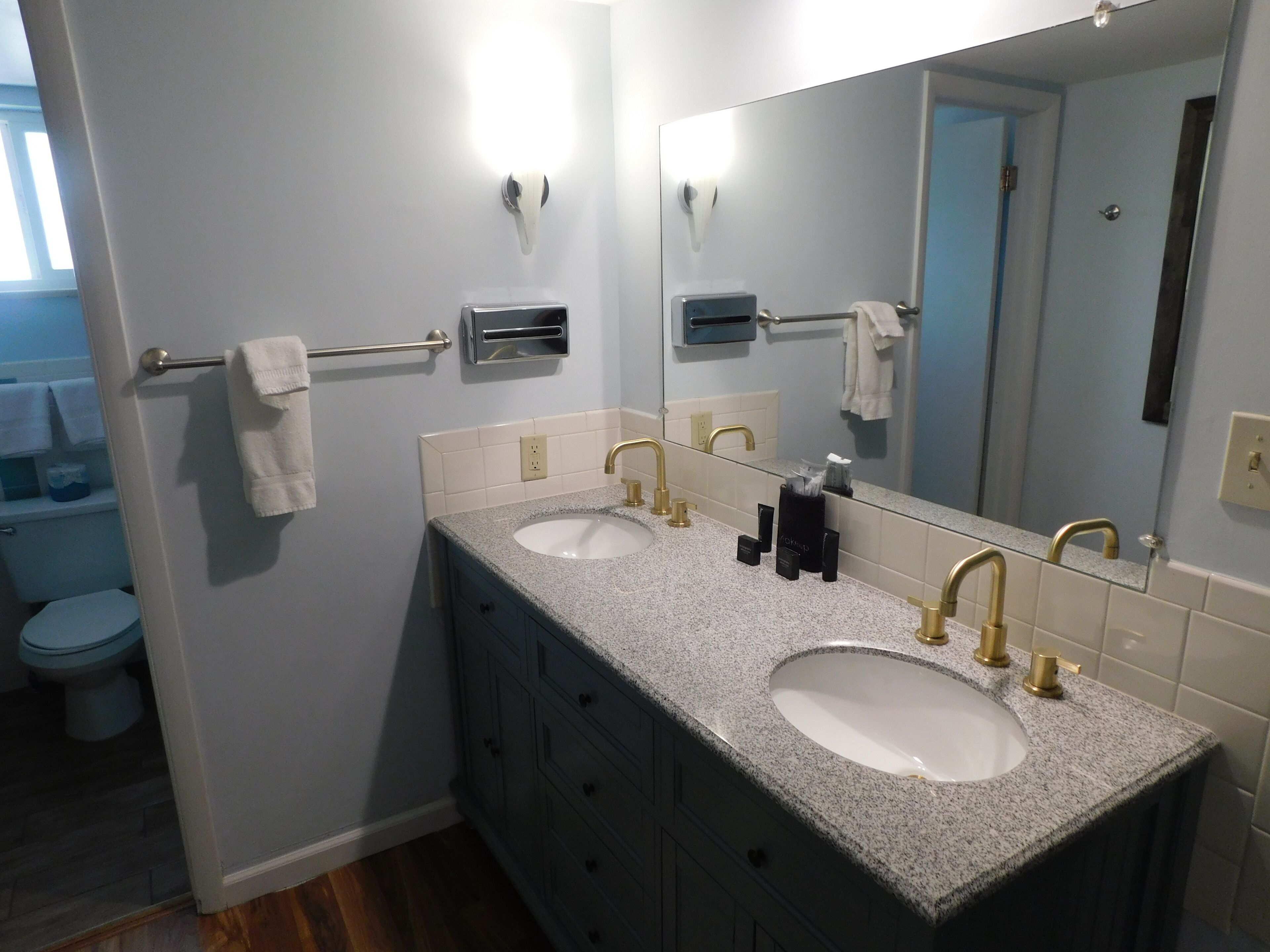 A bathroom with two sinks, a towel rack, a mirror, and a toilet.