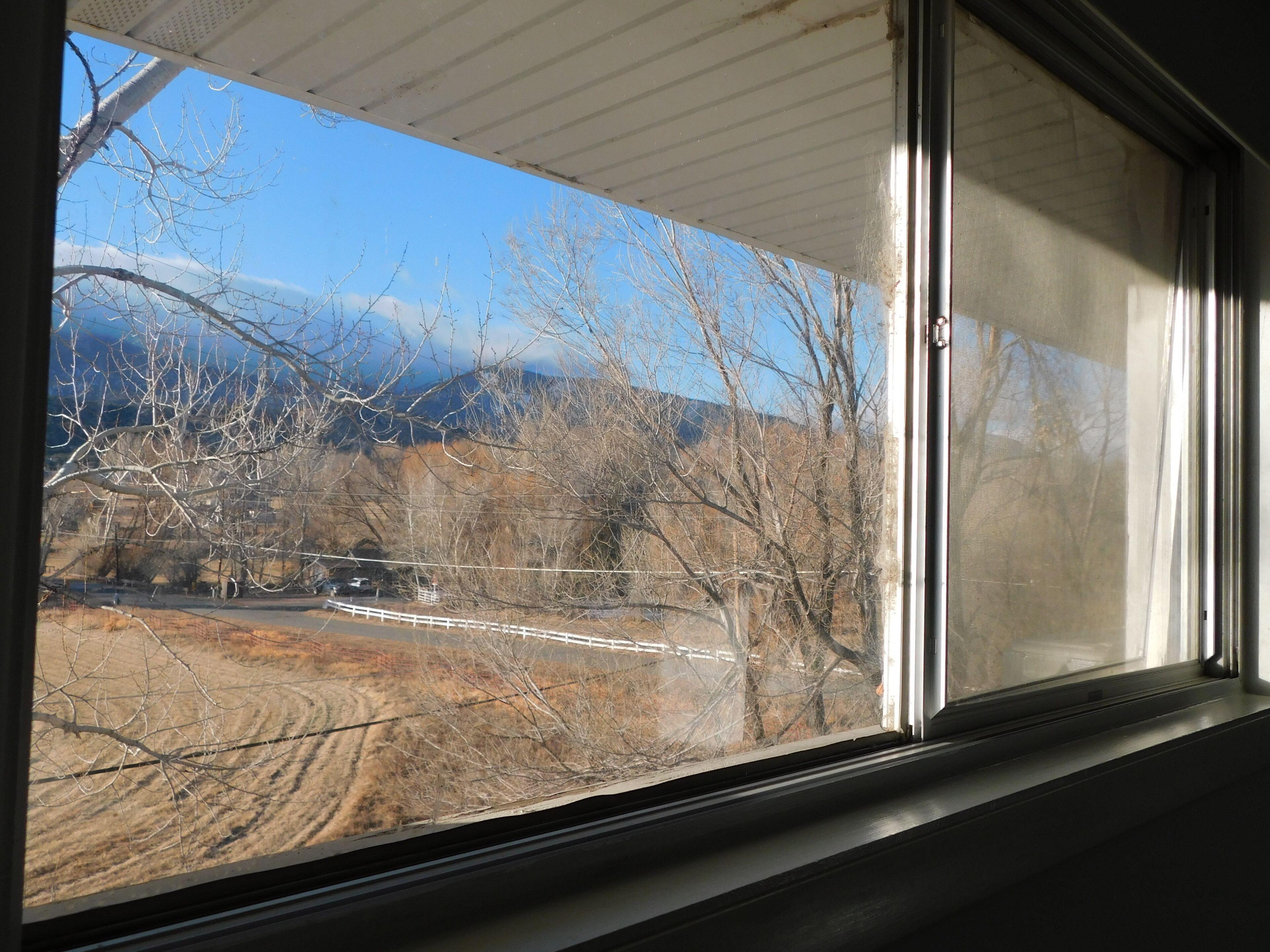 A window with a view of a mountainous landscape, a dirt road, and leafless trees.