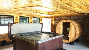 A wooden cabin interior with a hot tub, stone wall, and large windows. - Silver Ridge Lodge (Salida)