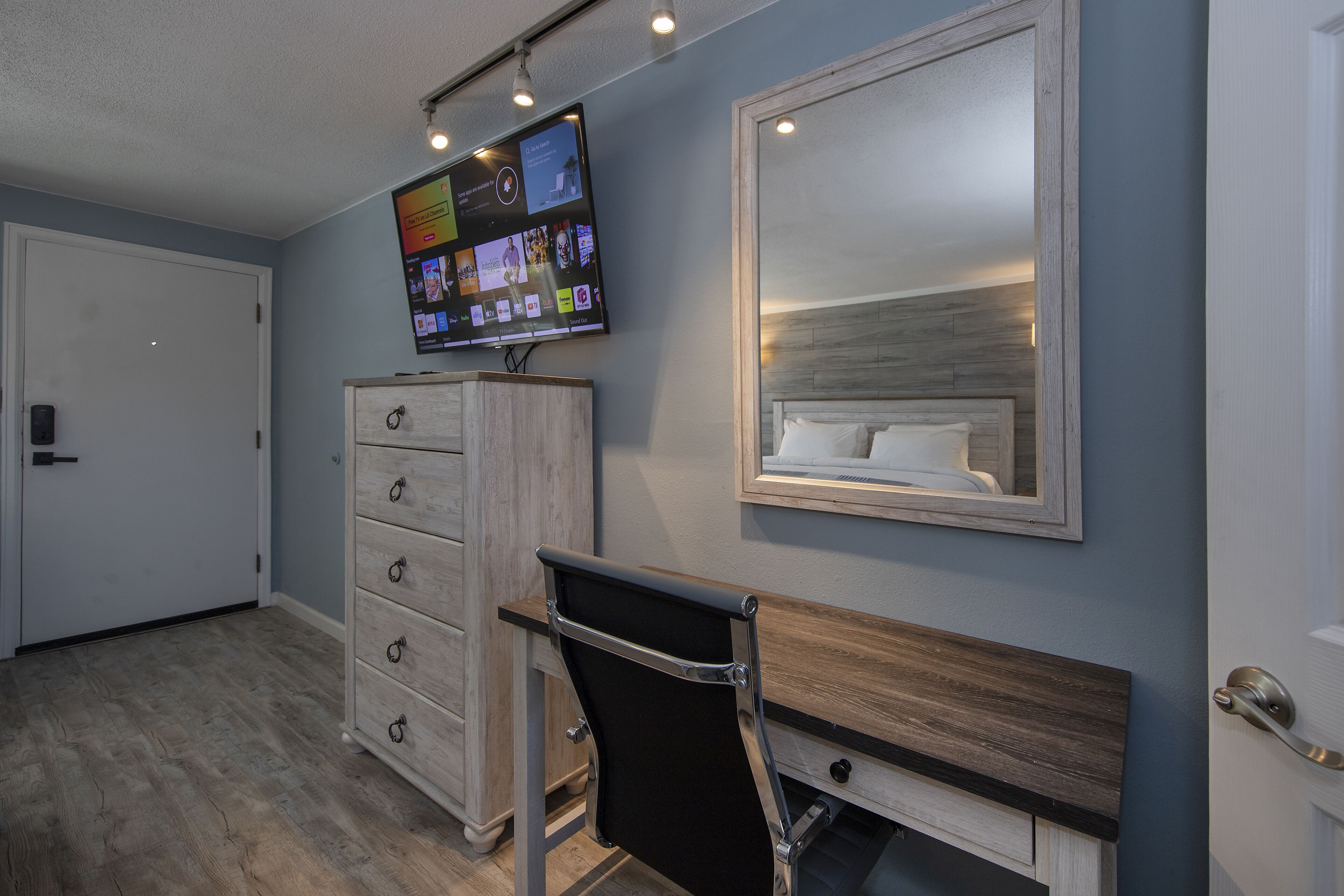 Une chambre à coucher avec un lit, une commode, un téléviseur fixé au mur et un miroir au-dessus du lit.
