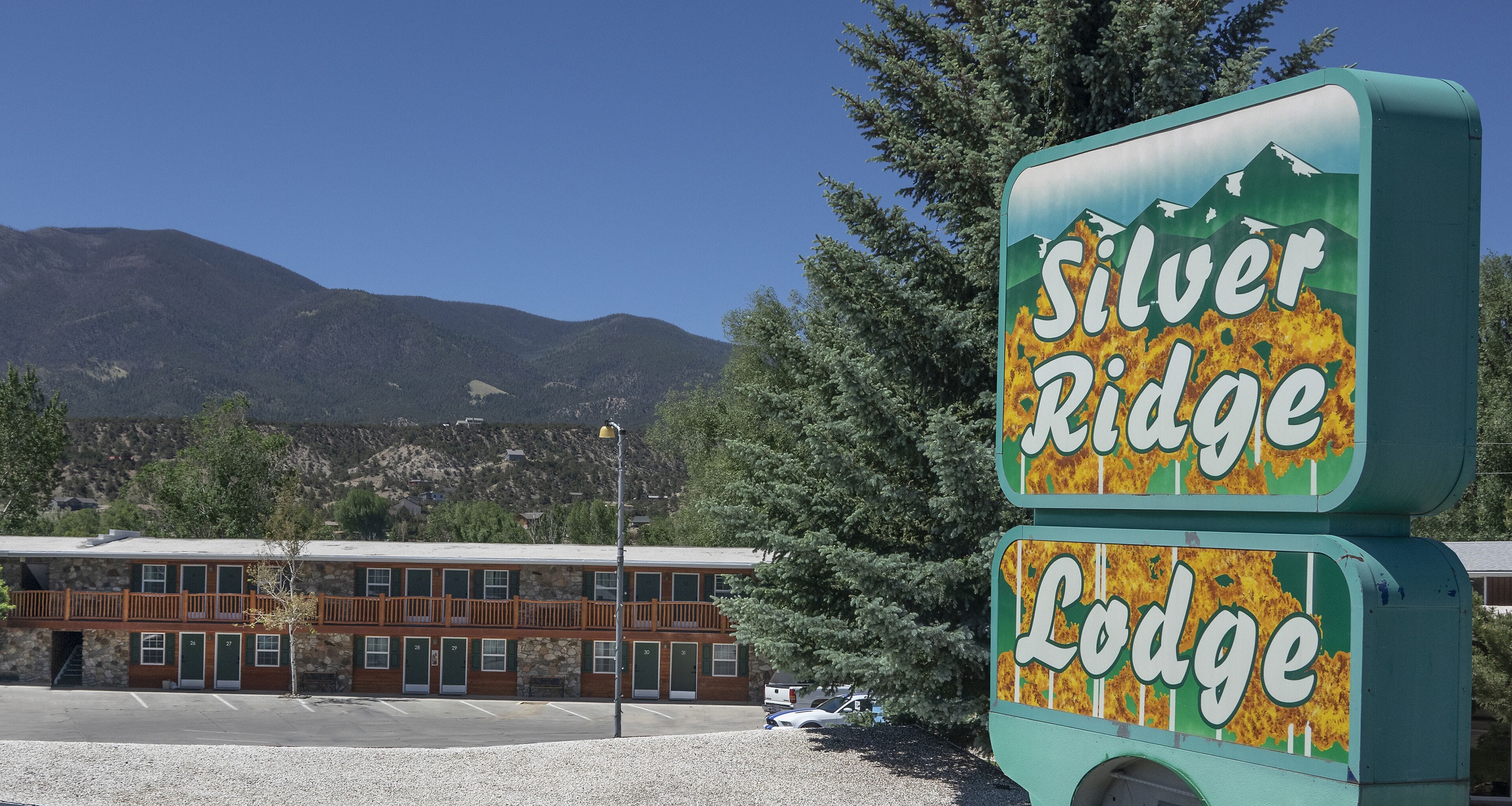Une enseigne de motel sur laquelle on peut lire « Silver Ridge Lodge », avec en arrière-plan des montagnes et un bâtiment comprenant plusieurs chambres.