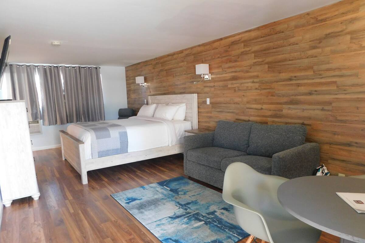 Ein Schlafzimmer mit einem Bett, einem grauen Sofa, einem kleinen runden Tisch und einem blau gemusterten Teppich.
