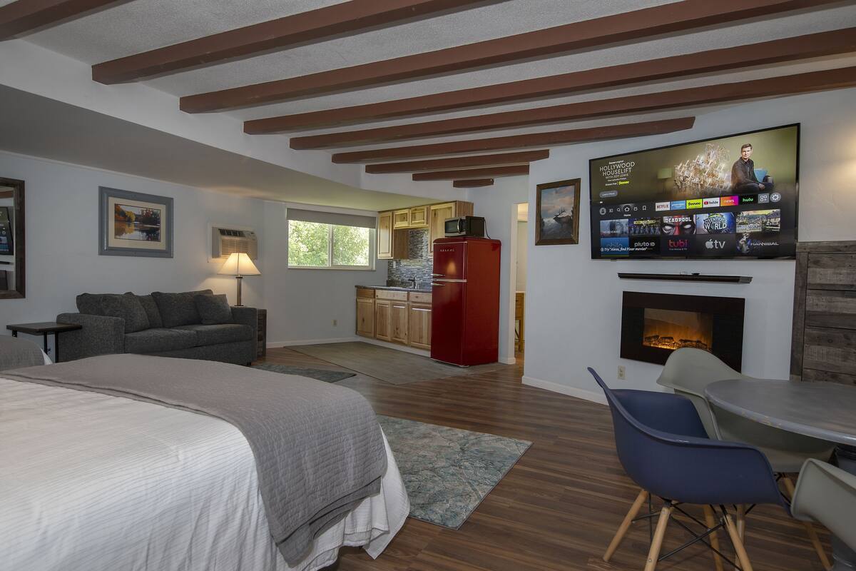 Ein modernes Schlafzimmer mit einem großen Bett, einem an der Wand befestigten Fernseher, einer Küchenzeile und einem Kamin.