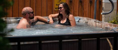 Una pareja en un jacuzzi, con un cartel de precaución al fondo.