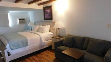 Una camera da letto con un letto, lampade sui comodini, un pavimento in legno e un divano grigio.