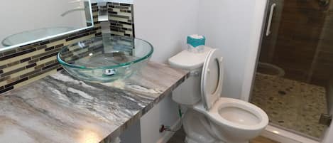 Un baño con lavamanos de cristal, inodoro y zona de ducha.
