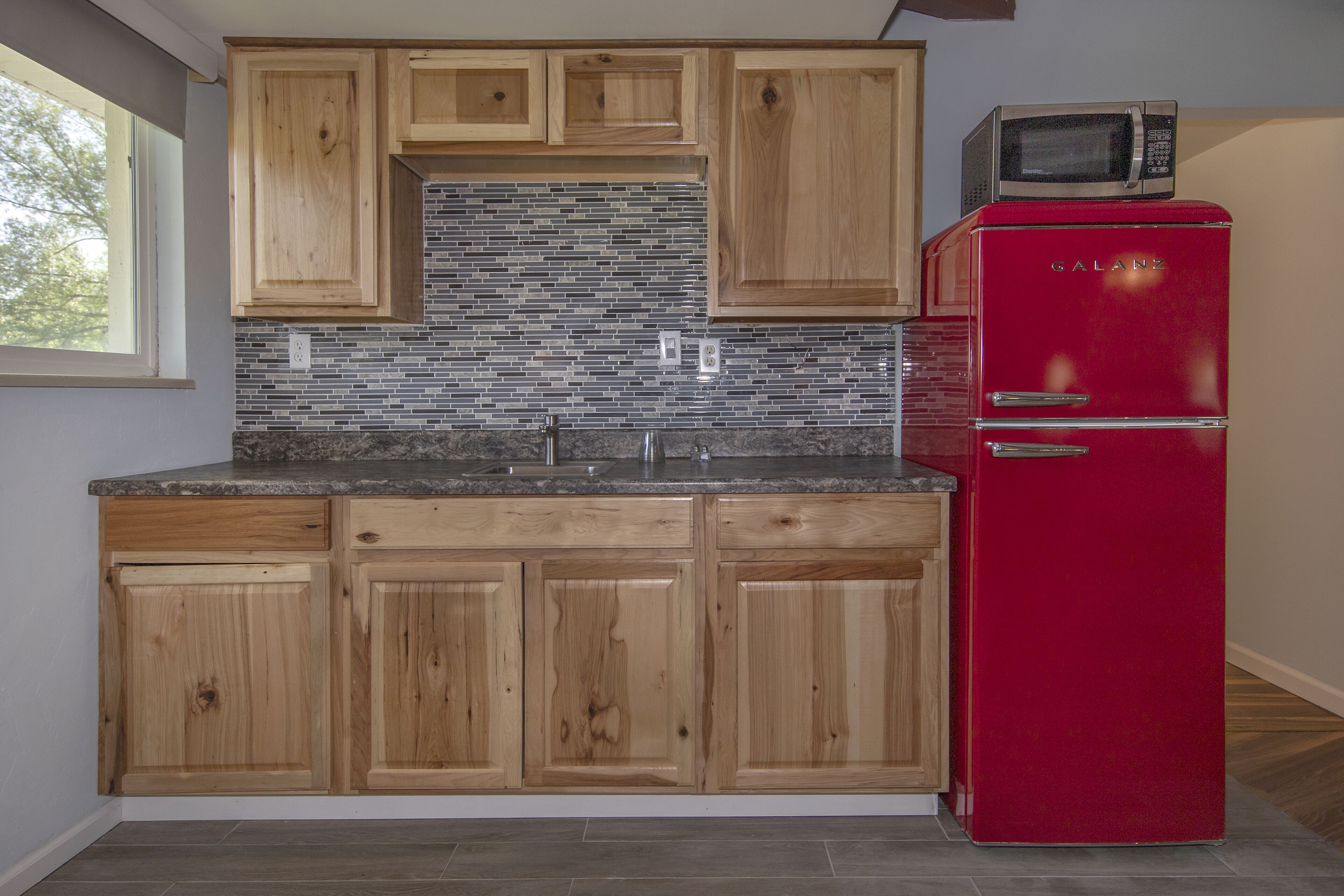 A kitchen with wooden cabinets, a red refrigerator, and a microwave on top.