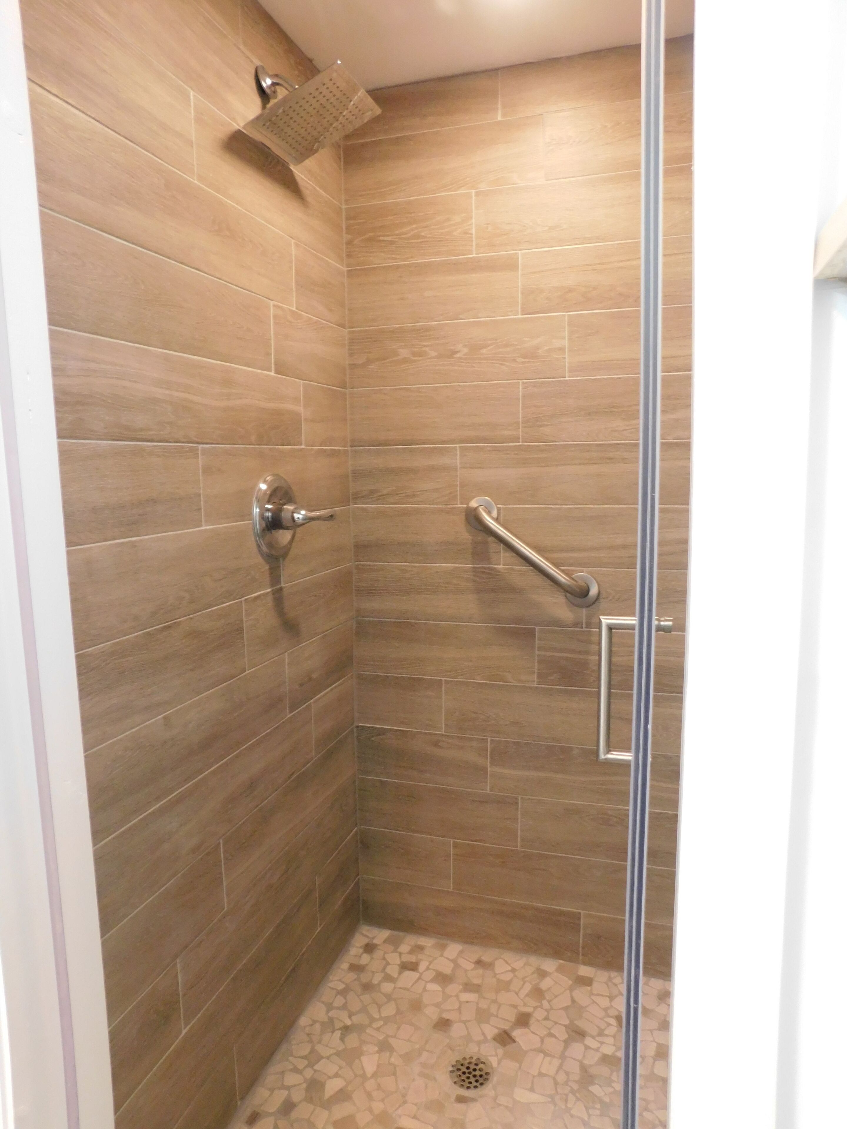 A shower with a glass door, a handrail, and a showerhead.