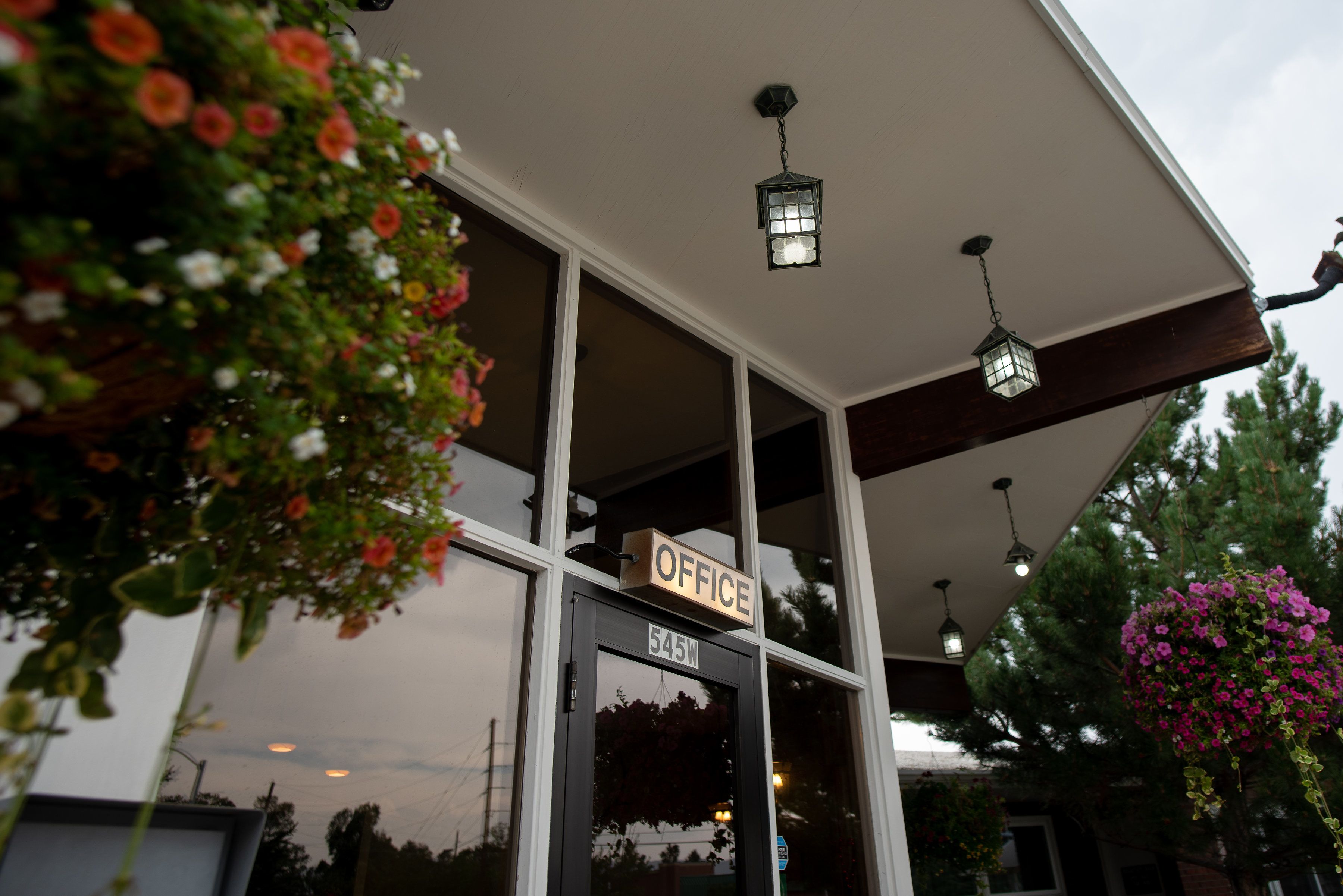 A building with a sign labeled "OFFICE" above the entrance, a number "545W" on the door, and hanging flower baskets.