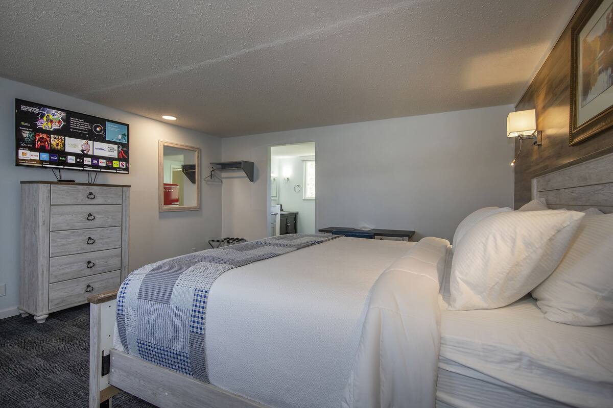 Ein Hotelzimmer mit Bett, Schminktisch, Wandfernseher und Spiegel.