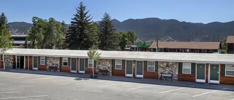 A motel with a row of rooms, a parking lot, and mountains in the background.