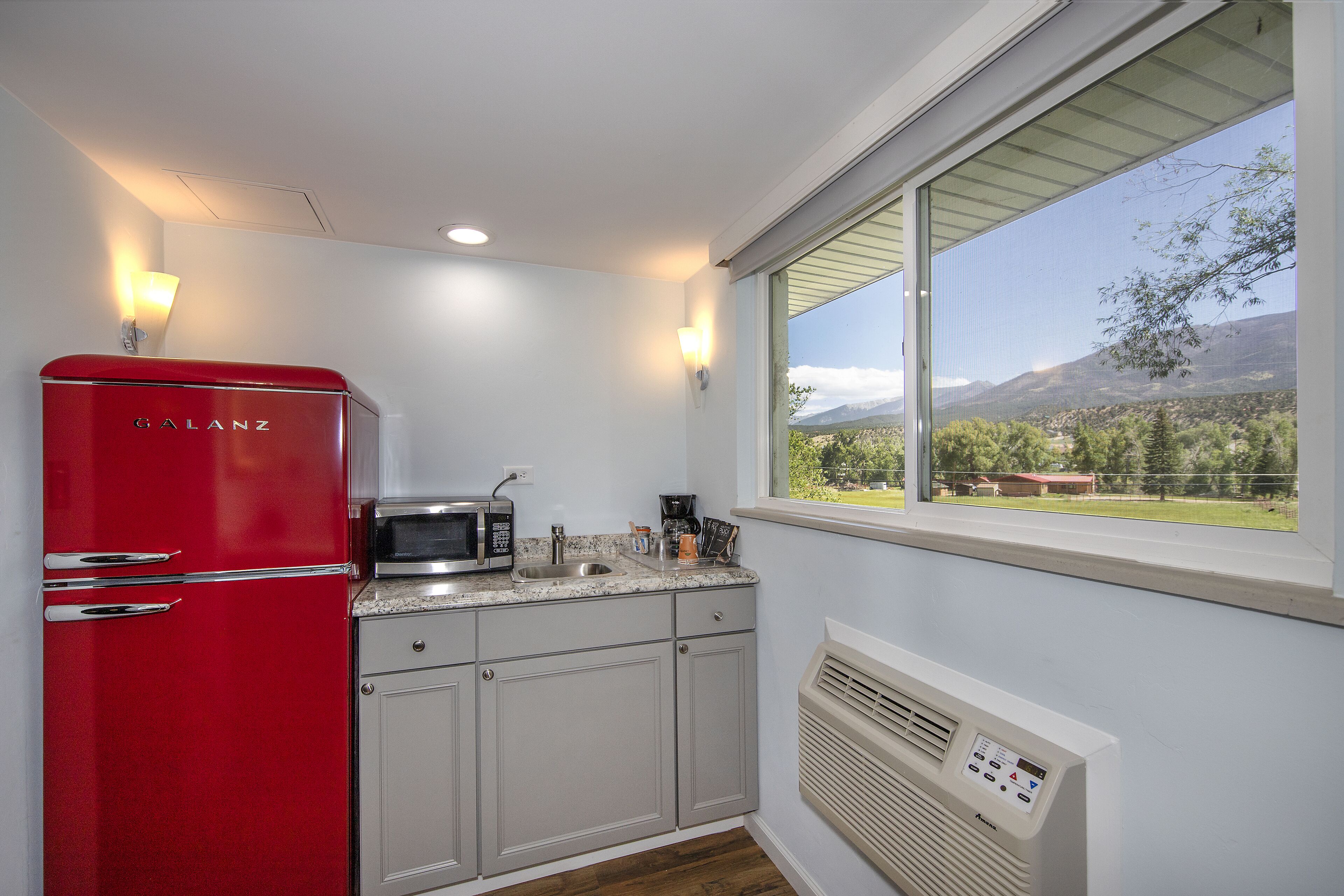 Una cocina con un refrigerador rojo, un microondas y un lavamanos.
