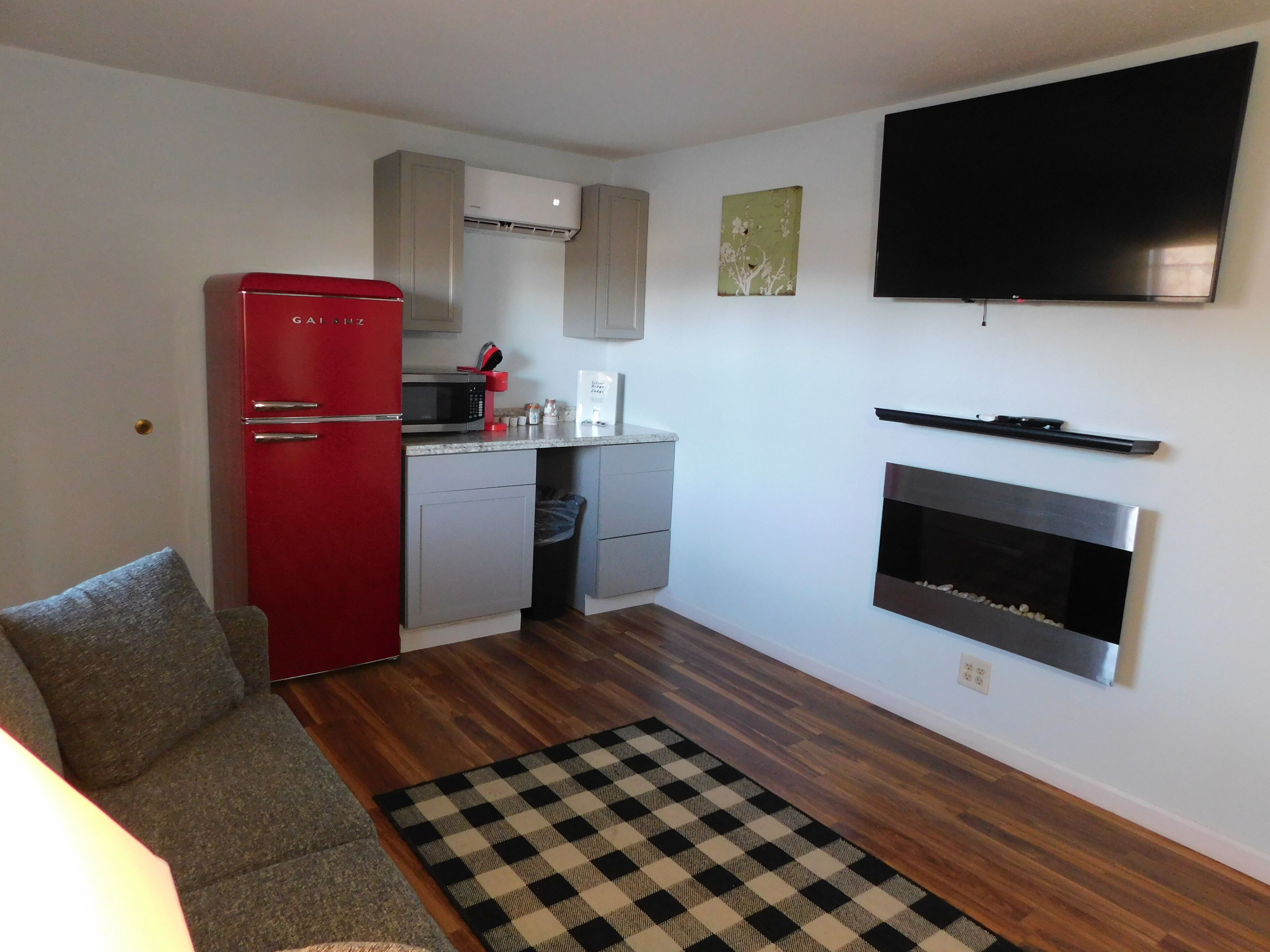 A compact kitchen with a red refrigerator, microwave, and a built-in oven. There's a flat-screen TV mounted on the wall and a fireplace below it.