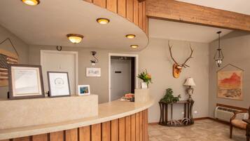 A reception area with a wooden reception desk, framed certificates, a wall-mounted deer head, and a painting.