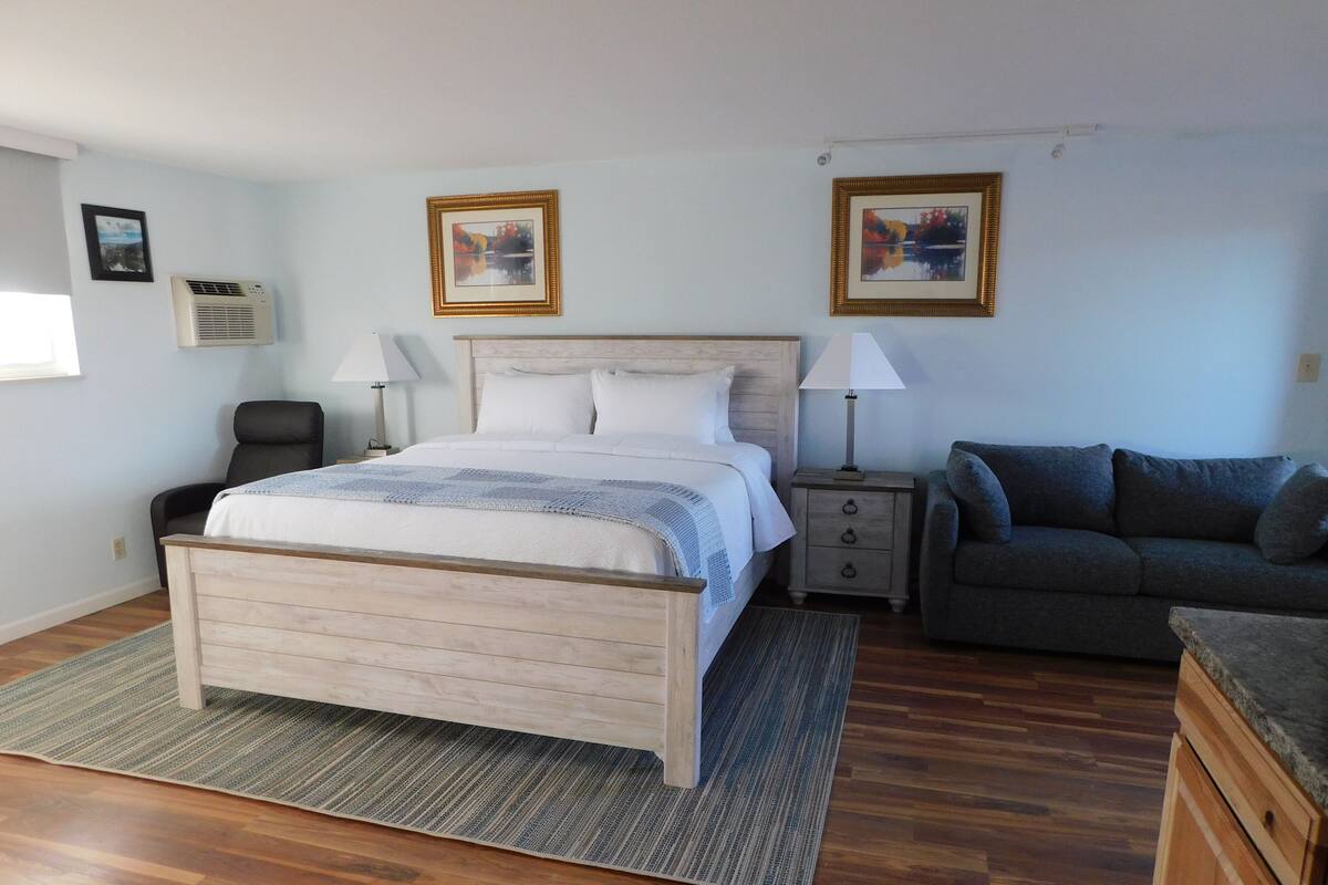 Ein Schlafzimmer mit einem hölzernen Bett, einem grauen Sofa, einem Nachttisch und zwei Wandleuchten.