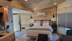 A modern bedroom with a wooden ceiling, a bed with white bedding, a nightstand, a chair, and a window with blinds. - Silver Ridge Lodge (Salida)