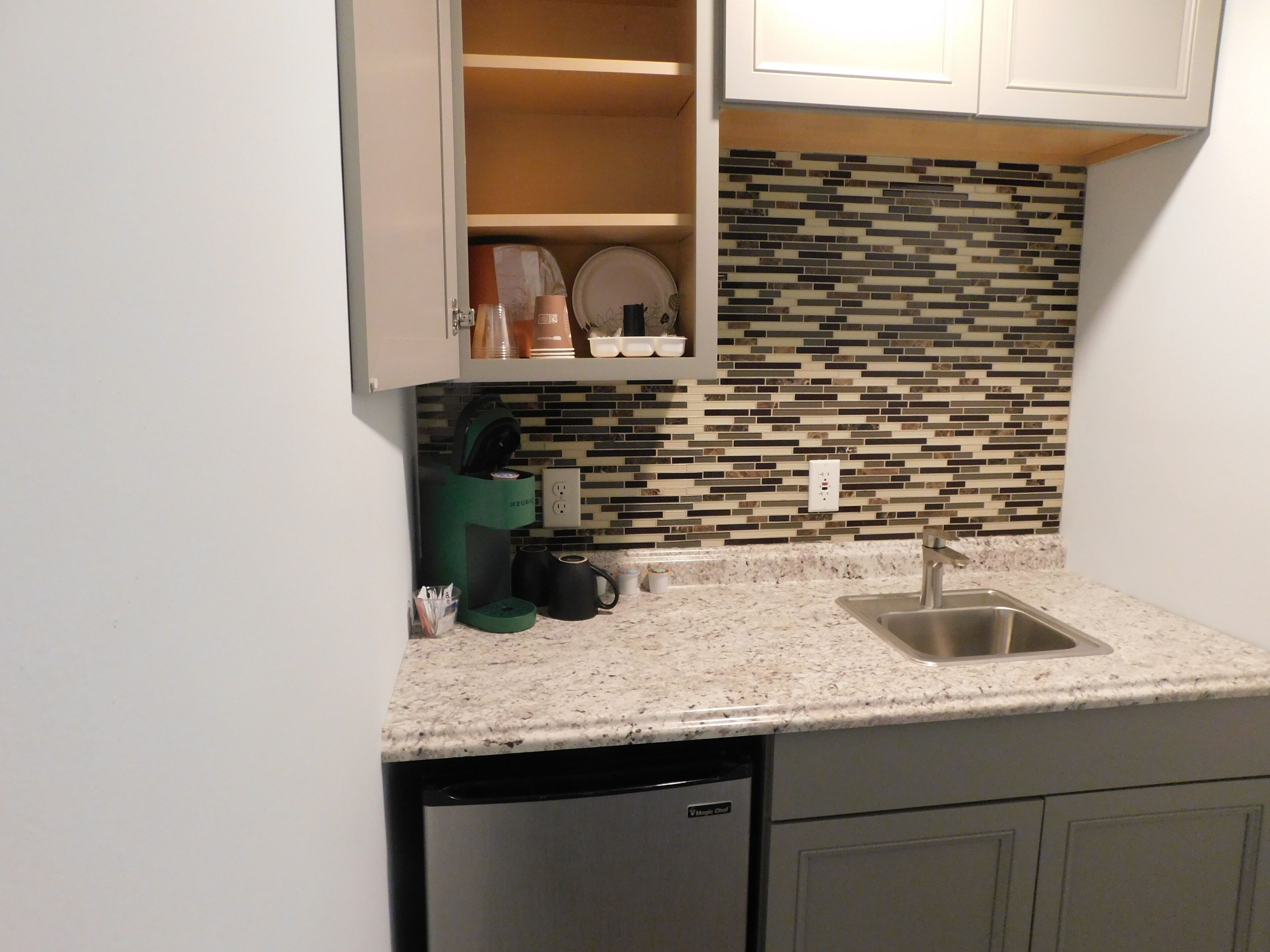 A compact kitchen with a built-in dishwasher, a coffee maker, and a tiled backsplash.