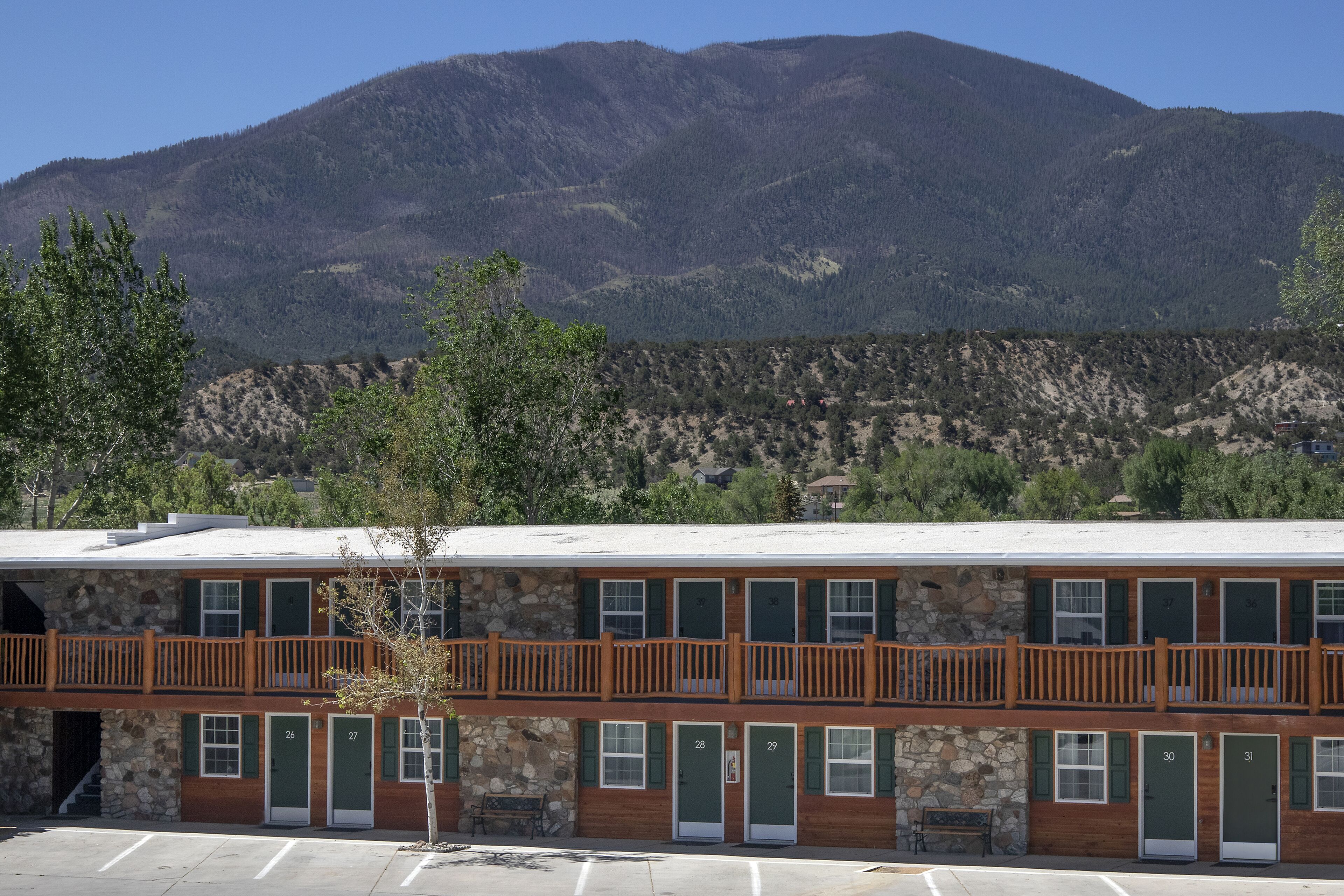 Un motel à deux étages, avec des chambres numérotées, un balcon et un paysage montagneux en arrière-plan.