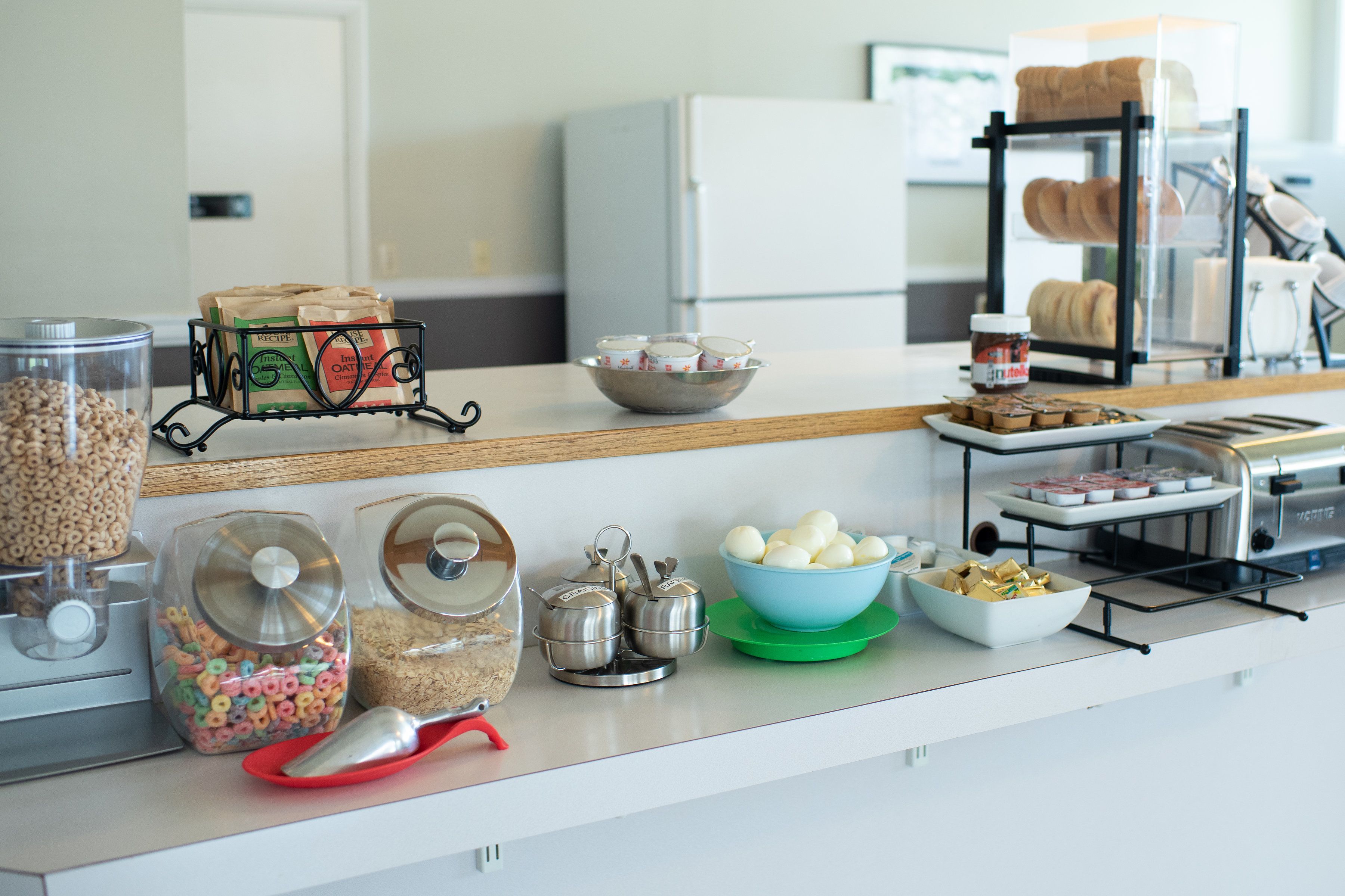 A kitchen counter with various food items and containers, including a bowl of eggs, jars of cereal, and a bread rack.
