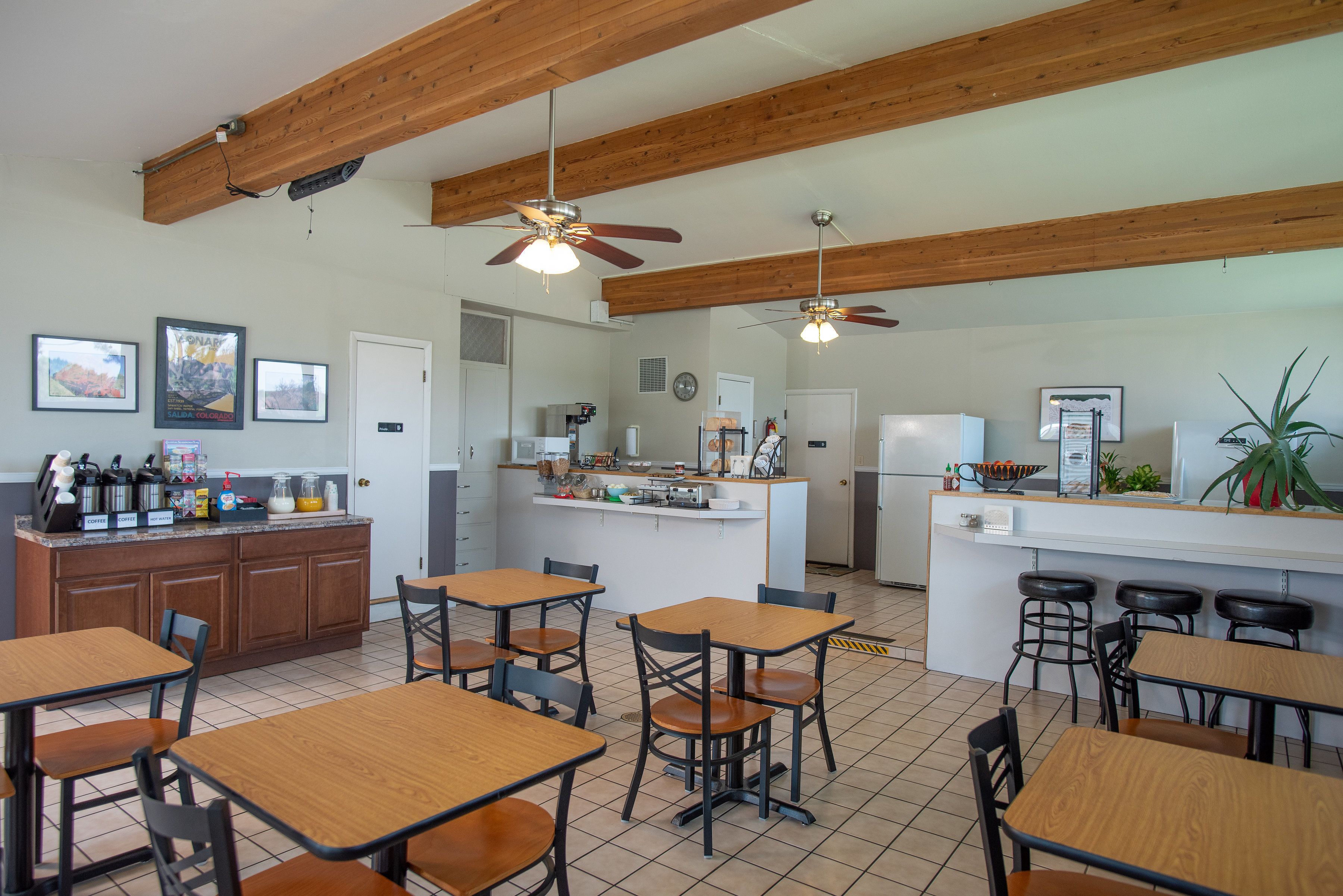 A restaurant with wooden ceiling beams, a central island with stools, and multiple tables and chairs.