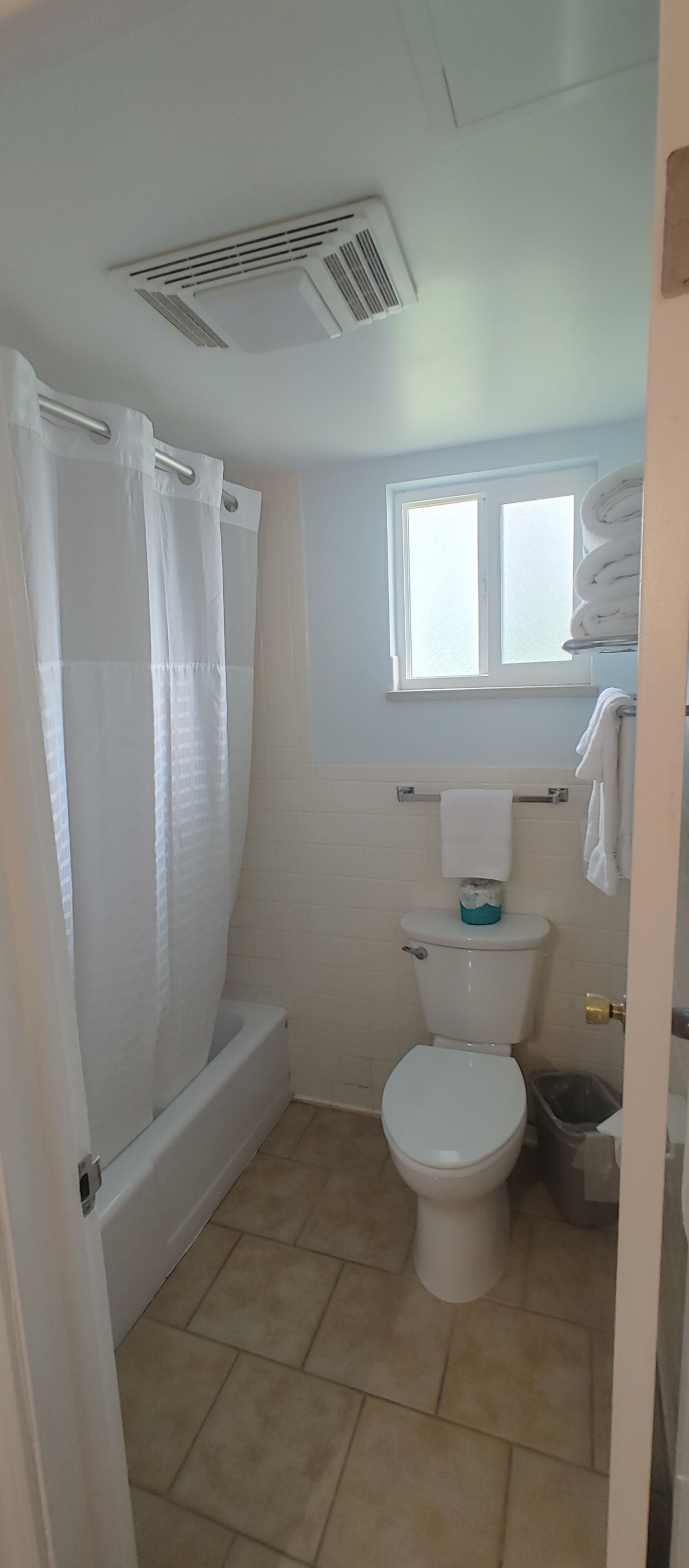 Ein Badezimmer mit Badewanne, Toilette und einem Fenster über der Toilette.