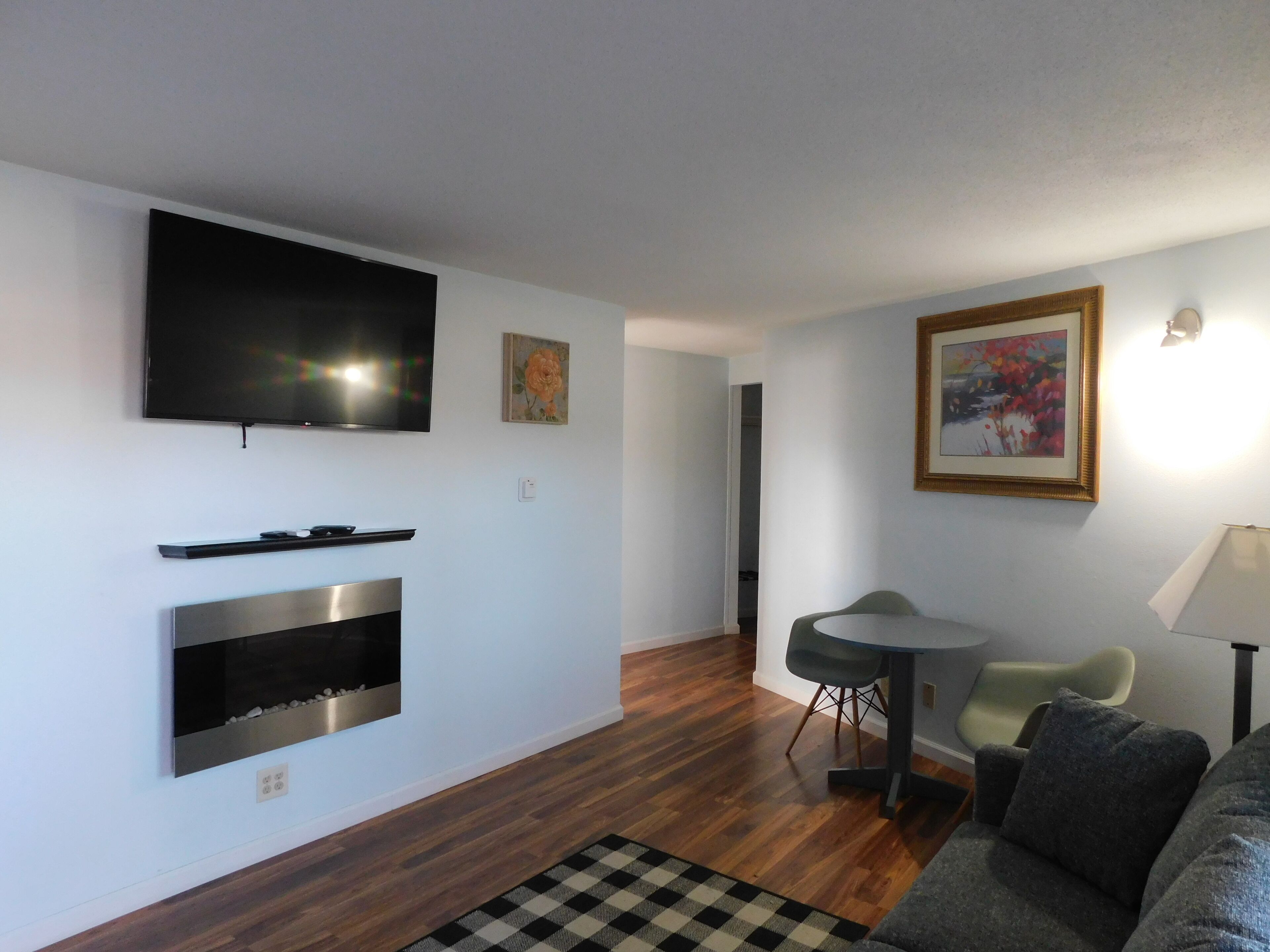 A modern living room with a flat-screen TV, a fireplace, a dining area with a table and chairs, and artwork on the walls.