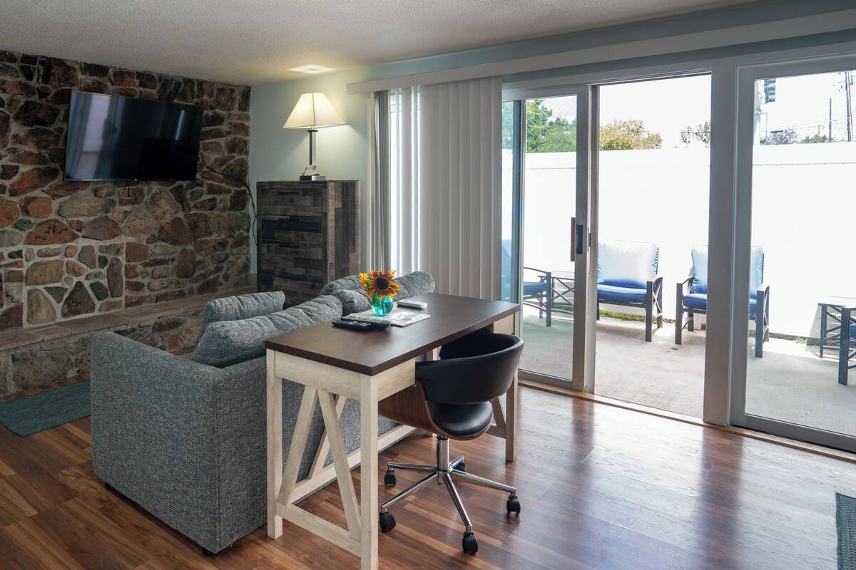Ein Wohnzimmer mit Steinwand, Flachbildfernseher, Sofa, Couchtisch und einer Glastür zum Außenbereich.