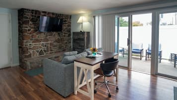 A living room with a stone wall, a flat-screen TV, a sofa, a coffee table, and a sliding glass door leading to an outdoor seating area.
