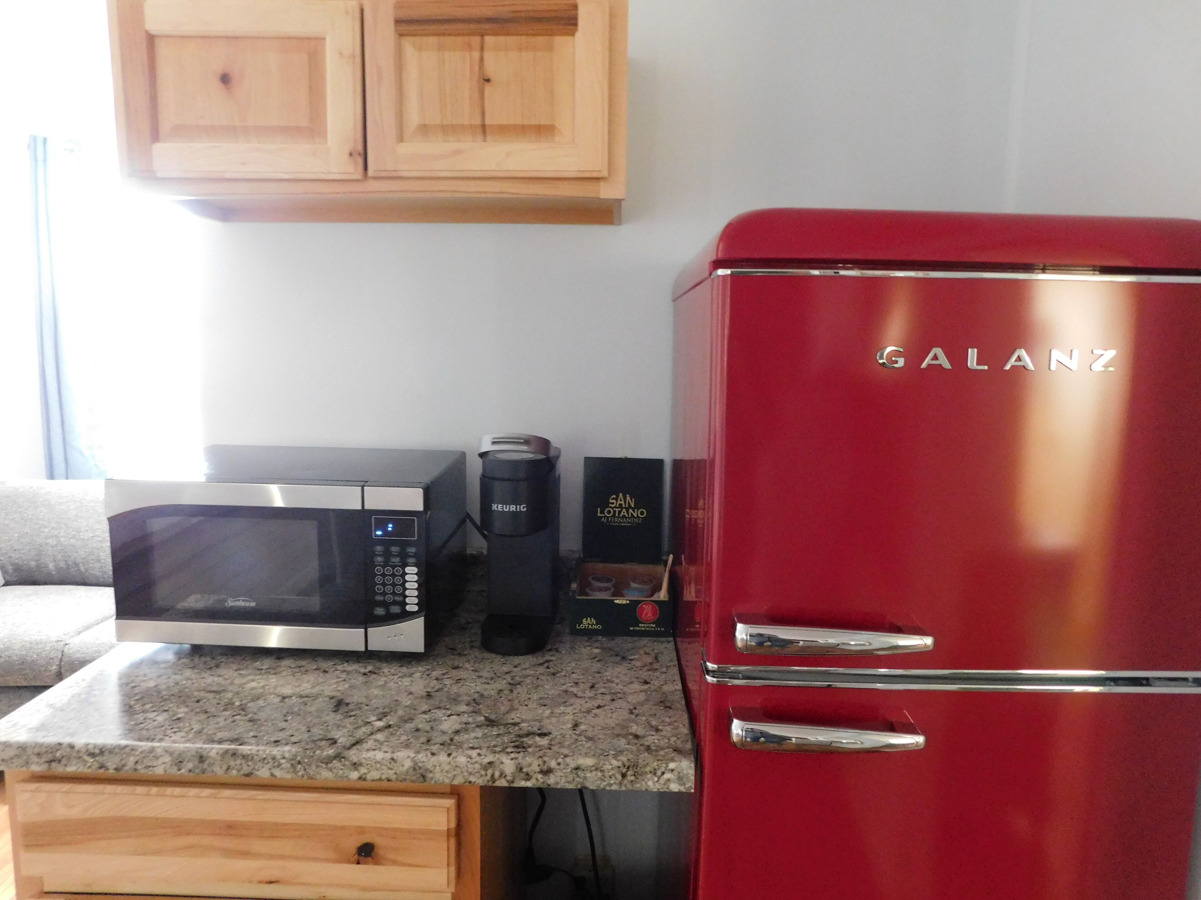 A kitchen with a red Galanz refrigerator, a black microwave, and a Keurig coffee maker on the countertop.