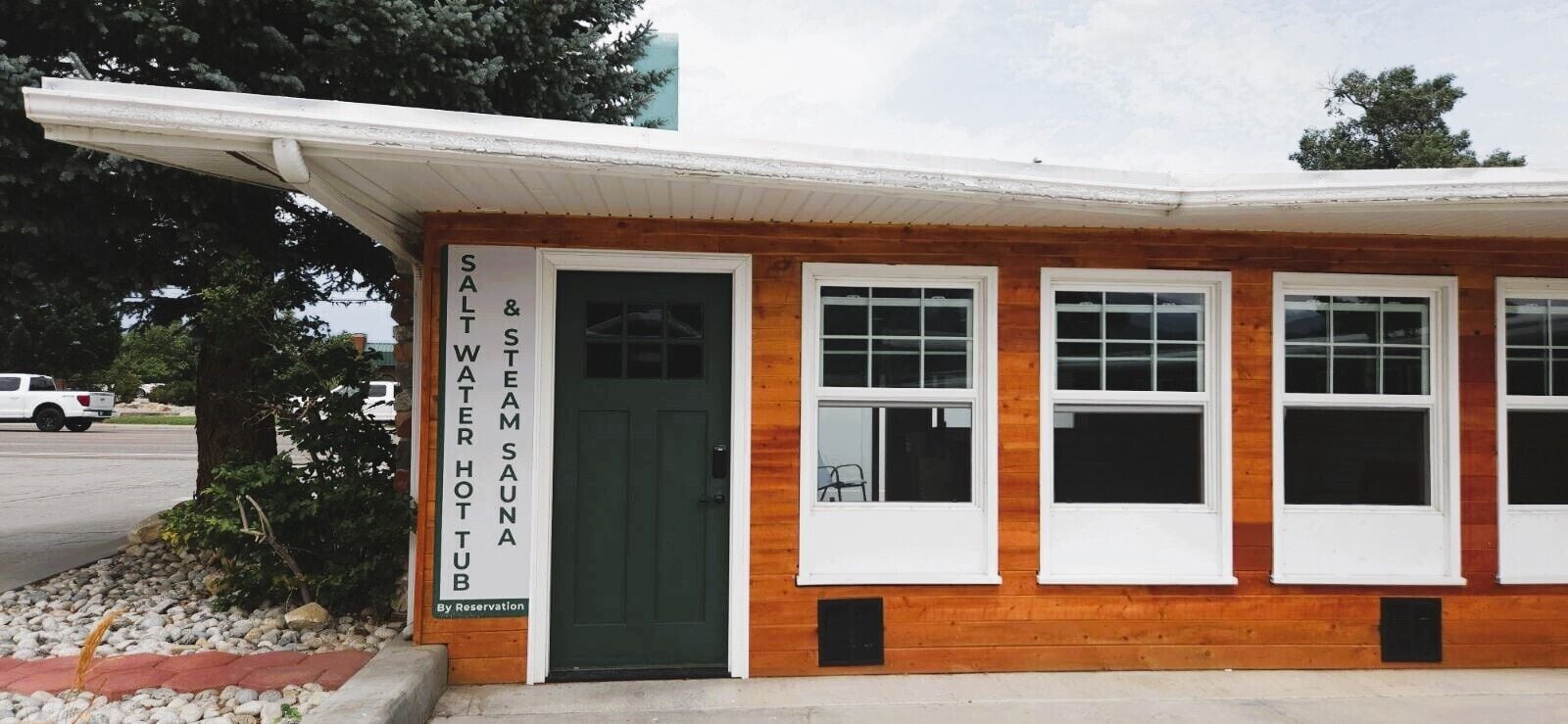 A wooden building with a green door and windows, labeled "Salt Water Sauna & Steam Hot Tub."