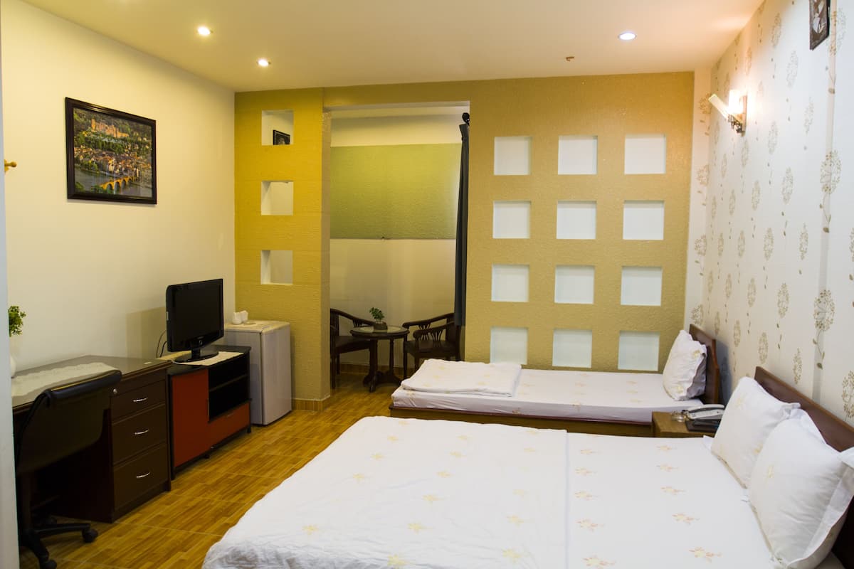 Ein Hotelzimmer mit zwei Betten, einem Schreibtisch mit Computer, einem Sessel, einem kleinen Tisch und einem Bild an der Wand.