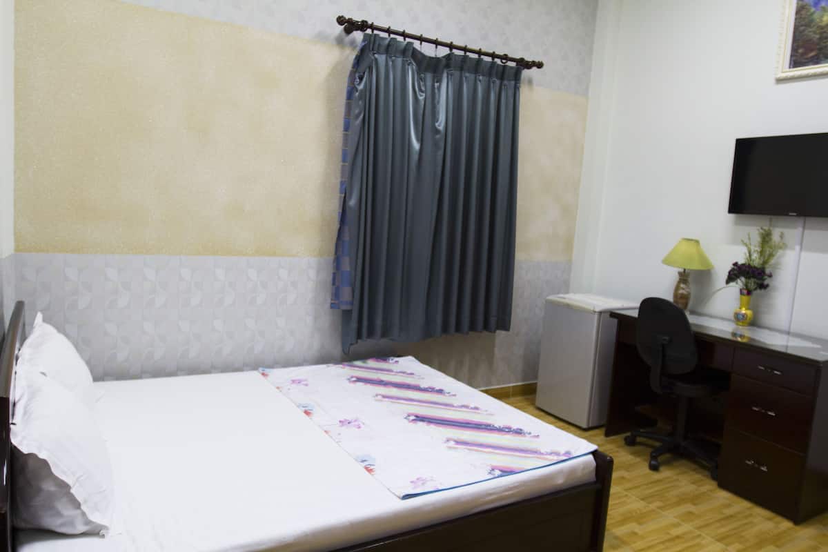 Ein Hotelzimmer mit Bett, Schreibtisch mit Stuhl, Fernseher und einem kleinen Tisch mit Lampe und Vase.
