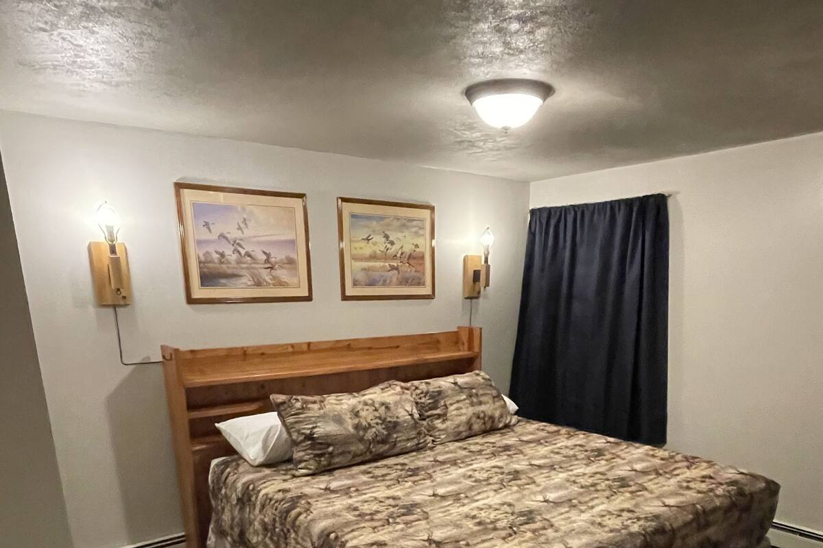 A bedroom with a wooden bed, two wall-mounted lights, and two framed pictures on the wall.