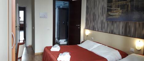 A hotel room with two beds, a shower, a painting on the wall, and a wooden floor.