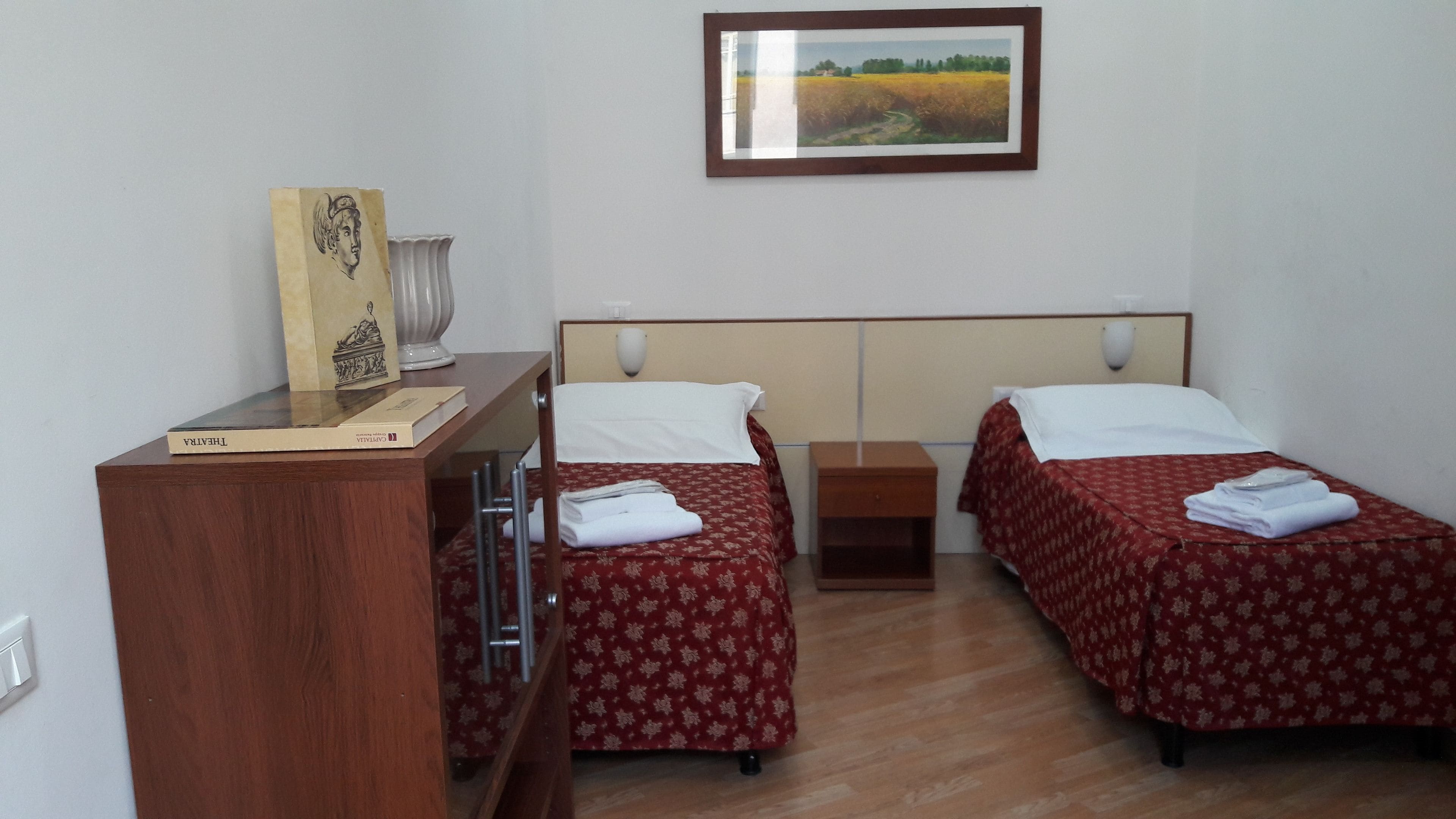 Habitación de hotel con dos camas, un escritorio, una silla, una lámpara y un cuadro en la pared.