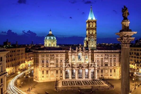 A grand historical building with a prominent clock tower and a dome, surrounded by a well-lit square. - San Vito Suites (Rome)