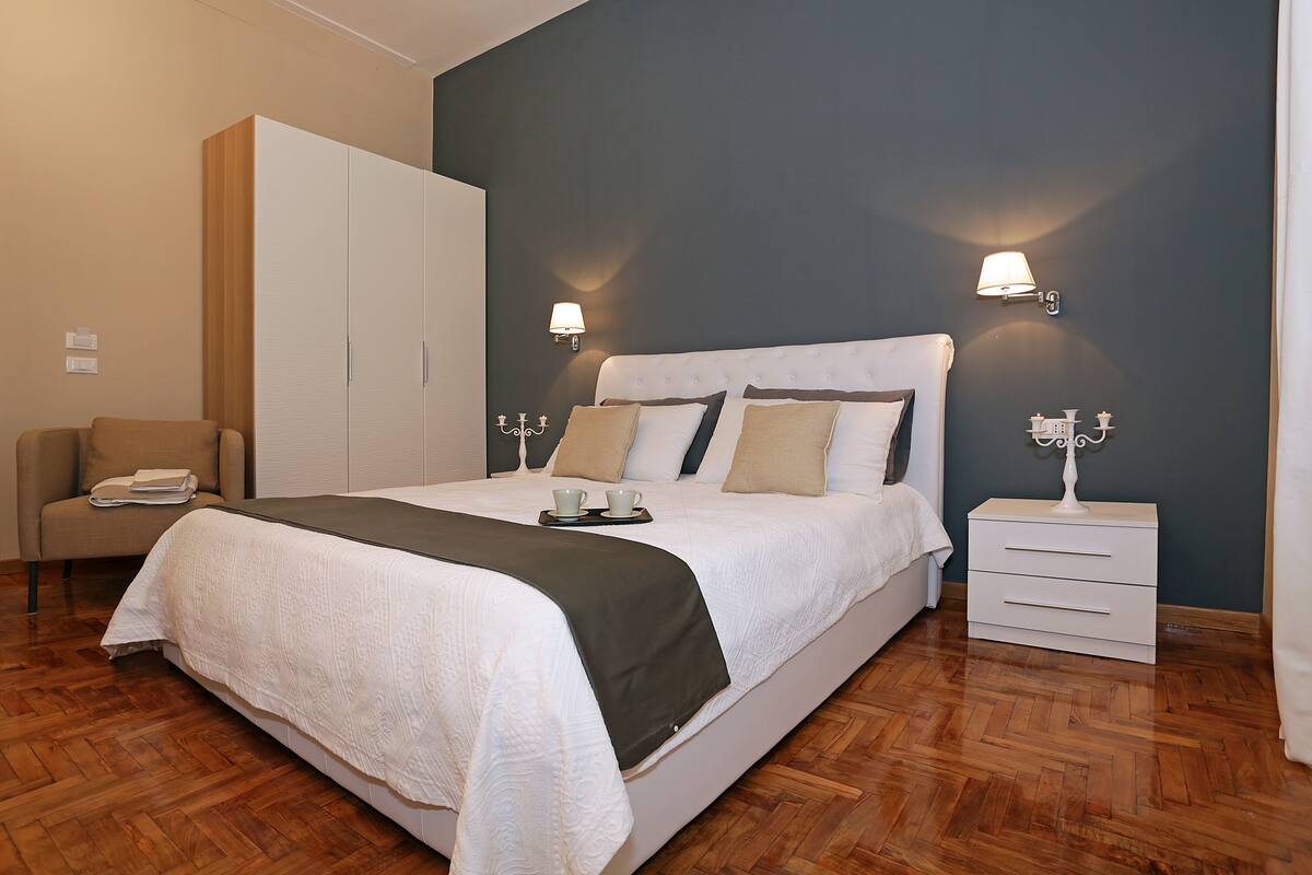 A modern bedroom with a large bed, two bedside tables, a wardrobe, and a chair.