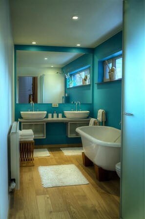 A modern bathroom with two sinks, a bathtub, and a large mirror.