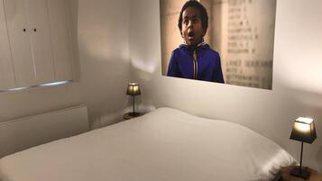 Een slaapkamer met een bed, twee bedlampjes, een raam met jaloezieën en een aan de muur hangend schilderij.