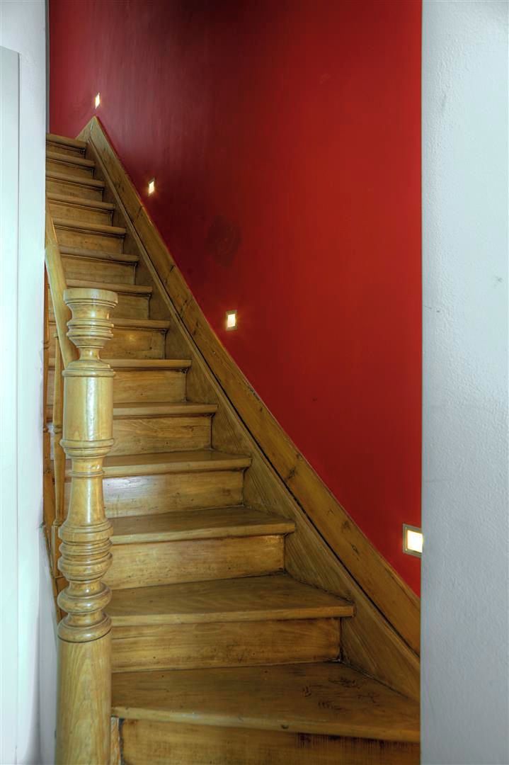 Un escalier en bois, avec un mur rouge d’un côté et un mur blanc de l’autre.